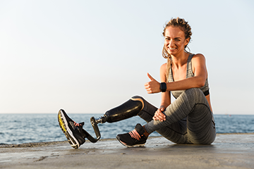 smiling woman with prosthetic leg by the beach giving thumbs up